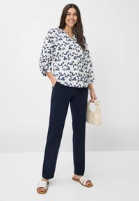 Blomstret bluse med marineblå blomster på hvid baggrund, trekvartærmer; parret med mørk marineblå lige bukser og hvide sandaler.