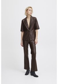 Blazer en cuir synthétique marron à manches courtes et fermeture à un bouton, associé à un pantalon ajusté assorti et des bottes à talons noires.