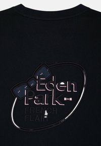 T-shirt en coton noir arborant un logo texturé avec une illustration d'un nœud papillon. Le texte "Eden Park FRENCH FLAIR" est inscrit dans des couleurs contrastées.