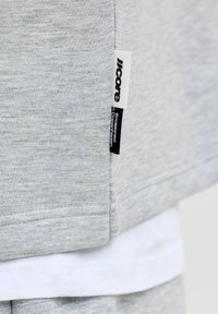 Gros plan sur un tissu gris avec une étiquette de vêtement blanche et noire portant la mention « core Envisioned Copenhagen » cousue sur la couture latérale.