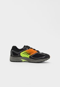 Svart sneaker med mesh-overdel, oransje og neongrønne aksenter, og grå gummisåle. Har snøring, polstret krage, og teksturert design.