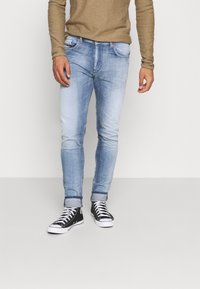 Vaaleansiniset farkut, joissa on slim fit -leikkaus, hieman haalistunut ulkonäkö, käärityt lahkeet ja viisi taskua, yhdistettynä mustiin lenkkareihin.