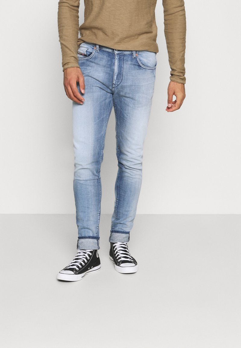 Vaaleansiniset farkut, joissa on slim fit -leikkaus, hieman haalistunut ulkonäkö, käärityt lahkeet ja viisi taskua, yhdistettynä mustiin lenkkareihin.