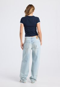 Navy t-shirt with white trim paired with light blue, loose-fitting jeans. T-shirt fabric appears smooth; jeans have a worn texture with visible pockets.