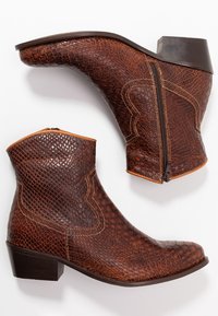 Un par de botas marrones hasta el tobillo con textura de reptil en relieve, cremallera lateral y tacón bajo, exhibidas sobre un fondo blanco.