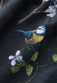 Czarna tkanina z kolorową ilustracją ptaka. Niebieski, zielony i żółty ptak siedzi wśród delikatnych kwiatów i zielonych liści.