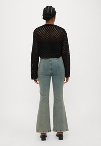 Maglione nero a maglia aperta, corto, con maniche lunghe, abbinato a jeans a zampa di elefante azzurri chiari con vita alta e dettagli di cuciture minimaliste.