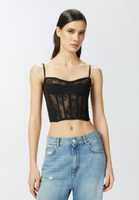 Crna čipkana kratka majica s tankim trakama, koja ima dekolte u obliku srca i strukturirani dizajn korpice; uparena s svijetloplavim derutnim trapericama.