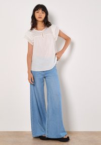 Hvid bluse med broderet hulmønster, nøglehuludskæring og korte ærmer, parret med lyseblå vide jeans og sorte platform sandaler.