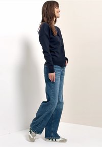 Cárdigan azul marino con botones, combinado con jeans de pierna recta azul claro y zapatillas con detalles verdes. Tela lisa, ajuste relajado.