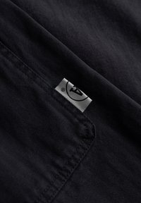 Sort stof med sildebensmønster; har et lille hvidt mærkat med et logo; glat tekstur; foldet og delvist synlig.