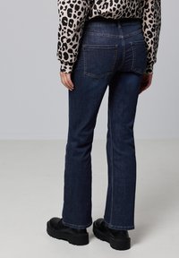 Vaqueros de mezclilla de un azul oscuro con un diseño de pierna recta, con bolsillos traseros y combinados con zapatos negros de suela gruesa. Suéter de estampado animal por encima.