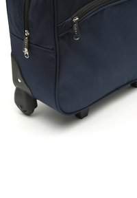 Navy modrý cestovní kufr se dvěma stříbrnými zipy, texturovaná tkanina, robustní černý základ a čtyři kolečka pro snadnou mobilitu. Kompaktní design pro pohodlí.