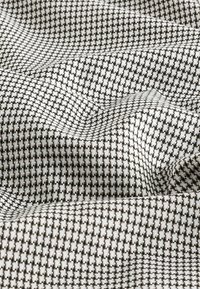 Textil cu un model carolat în alb și negru, având o textură țesută care creează adâncime și umbre subtile în material.