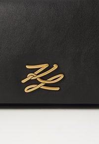Svart skinnkortholder med en glatt tekstur, med et fremtredende gull cursivlogo på forsiden. Minimalistisk design uten ekstra utsmykkinger.