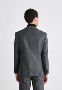 Blazer di lana grigia a trama con colletto nero, caratterizzato da una vestibilità sartoriale, una fessura singola e polsini con bottoni. La vista posteriore mostra una costruzione senza cuciture.