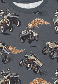 Sivá látka s ilustrovanými monster truckmi so plameňmi, šachovnicovými vlajkami a agresívnymi dizajnmi v rôznych farbách.