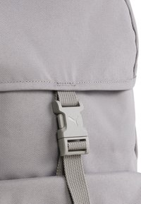 Grijze stoffen rugzak met een gestructureerde afwerking, stevige webbingriem en een plastic sluiting met een logo-detail.