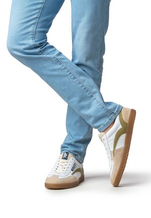 Zapatillas deportivas blancas y beige con detalles en verde, con un diseño de ante y cuero, atadas con cordones blancos, usadas con vaqueros azul claro.