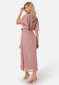 Robe longue en chiffon rose avec des manches courtes flottantes et une taille nouée. La robe présente un design fluide et un ourlet au genou.