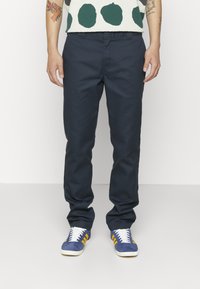 Chino blu marina in cotone, con vestibilità dritta, tasche anteriori e cuciture minime, abbinati a sneakers in suede blu con strisce gialle.
