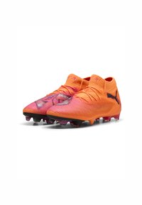Scarpini da calcio arancioni con una superficie strutturata, accenti in gradiente rosa e tacchetti multi-terreno neri e viola. Presentano un design aderente.