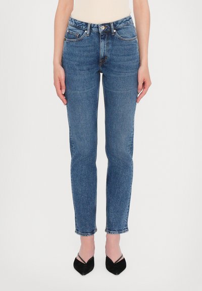 Blauwe denim jeans met hoge taille, aangesloten pasvorm, vijf-pocket ontwerp en rafelige zoom, gecombineerd met zwarte puntige hakken.