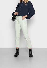 Navy button-up blouse with puff sleeves, paired with light green cropped jeans and black ankle boots with a silver ring accent.