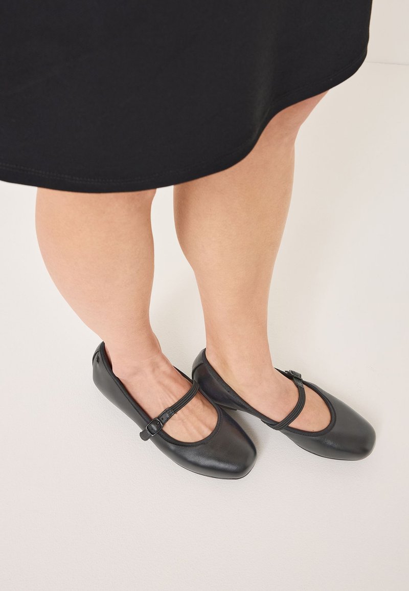 Schwarze flache Schuhe mit runder Spitze, ausgestattet mit einem dekorativen Riemen und einer Schnalle. Glattes, lederähnliches Material und minimalistisches Design.