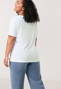 Weißes Kurzarm-T-Shirt mit lockerer Passform, Rundhalsausschnitt und weichem Baumwollmaterial, kombiniert mit hellblauen weit geschnittenen Hosen.