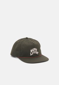 Oliven grønn baseballcaps med buet skjerm, prydet med hvit brodert tekst "BUSY LIVIN'" og en brun aksent langs skjermens kant.