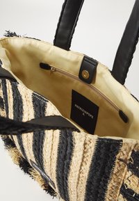 Borsa tote intrecciata in paglia con strisce nere e beige, dotata di manici in pelle e una tasca con zip. Interno foderato con etichetta del marchio visibile.