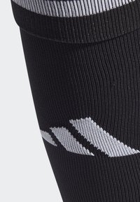 Calzino sportivo nero con texture a coste, caratterizzato da un motivo di logo bianco sul lato. La parte superiore ha una fascia a righe di contrasto.