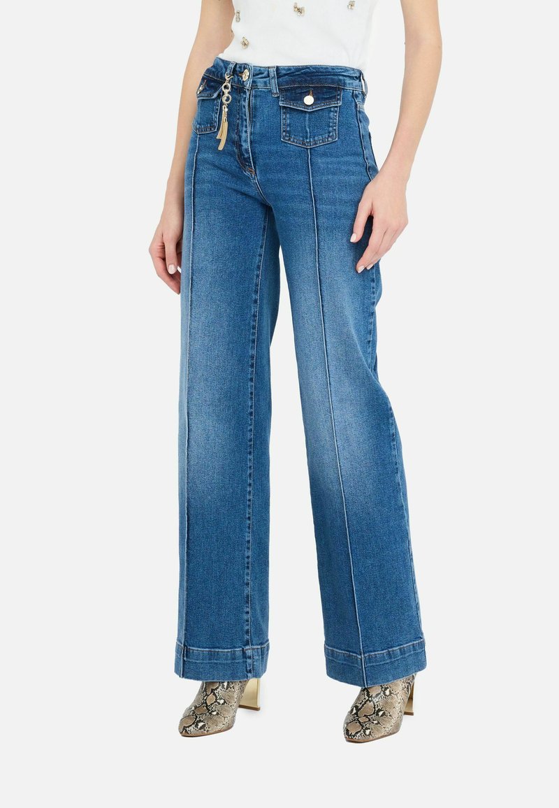 Jeans de mezclilla azul de pierna ancha y cintura alta, que cuentan con dos bolsillos frontales, un cierre dorado y acentuaciones decorativas en la parte delantera.