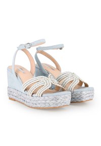 Sandalias de cuña de ante azul con plataforma de paja trenzada, tiras adornadas y hebilla en el tobillo. Textura suave con detalles decorativos.