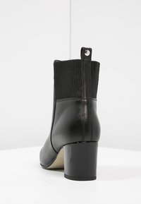 Bottine noire en cuir lisse avec une tige en tissu à côtes. Présente un talon épais et une languette à la arrière.