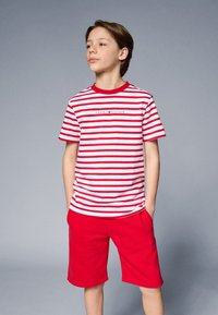 Rød og hvidstribet T-shirt med rund hals og logo, parret med ensfarvede røde shorts. Glat tekstur, afslappet design.