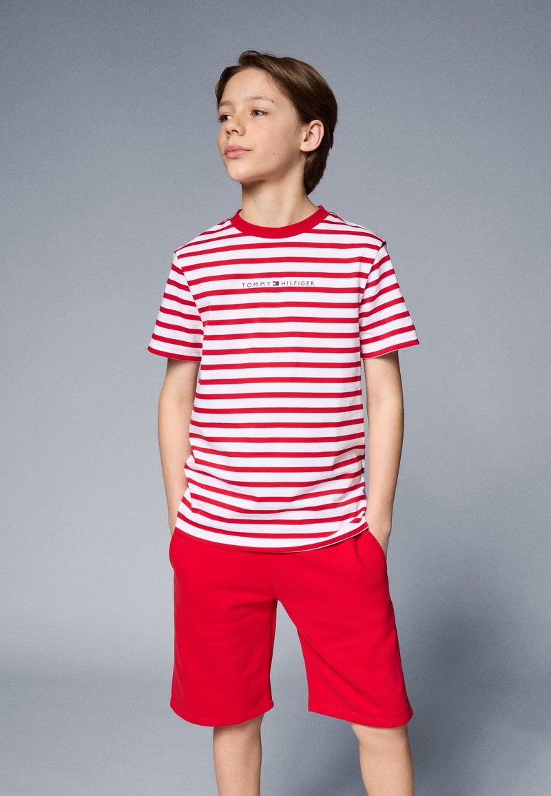 Rød og hvidstribet T-shirt med rund hals og logo, parret med ensfarvede røde shorts. Glat tekstur, afslappet design.