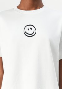 White cotton t-shirt featuring a black embroidered smiley face on the chest. Smooth texture, classic crew neck, and short sleeves.