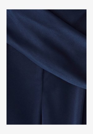 Tissu bleu marine foncé avec une texture lisse, présentant des plis drapés et un éclat prononcé, disposé en couches superposées.