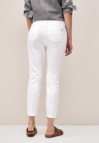 Pantalones de mezclilla blancos con un ajuste slim, que cuentan con dos bolsillos traseros y puños enrollados. Combinados con sandalias marrones y una camiseta gris.
