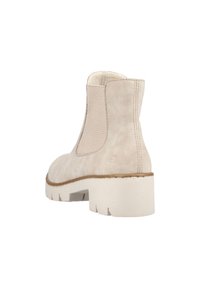 Bottine en suede beige avec des panneaux élastiques sur les côtés, un bout rond et une semelle en caoutchouc blanche épaisse, présentant un logo en relief discret sur le talon.