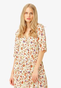 Floral dress in cream fabric featuring orange, purple, and green patterns. V-neckline and short, loose sleeves with a gathered waist.