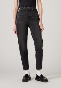 Black high-waisted jeans with a straight leg fit, denim material, minimal detailing, finished with cuffed hems and paired with black loafers.
