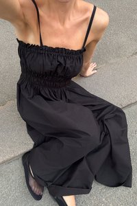 Robe noire sans manches en tissu léger, avec un corsage froncé et une jupe large et fluide. Portez avec des chaussures plates noires.