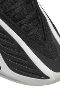 Musta lenkkari, jossa on verkkomateriaali kärjessä, mustat nauhat ja valkoinen pohja, jossa on kerroksellisia mustia kuvioita.