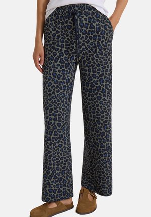 Pantalon ample avec imprimé léopard bleu et noir, taille élastique avec cordon, porté avec des chaussures marron à boucle et un haut blanc.