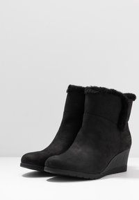 Botas negras con cuña hasta el tobillo, hechas de ante texturizado, con un suave y esponjoso puño y suela de goma. Presentan un sutil logo en el lateral.