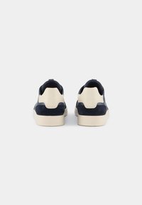Granatowe zamszowe sneakersy z beżowymi akcentami, charakteryzujące się gładką teksturą, zaokrąglonym kształtem i niskoprofilową gumową podeszwą. Dwie pętle na pięcie.