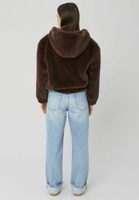 Veste courte en fausse fourrure marron avec capuche, associée à un jean à jambes larges bleu clair. Le jean présente un revers roulé et des coutures de poche arrière.